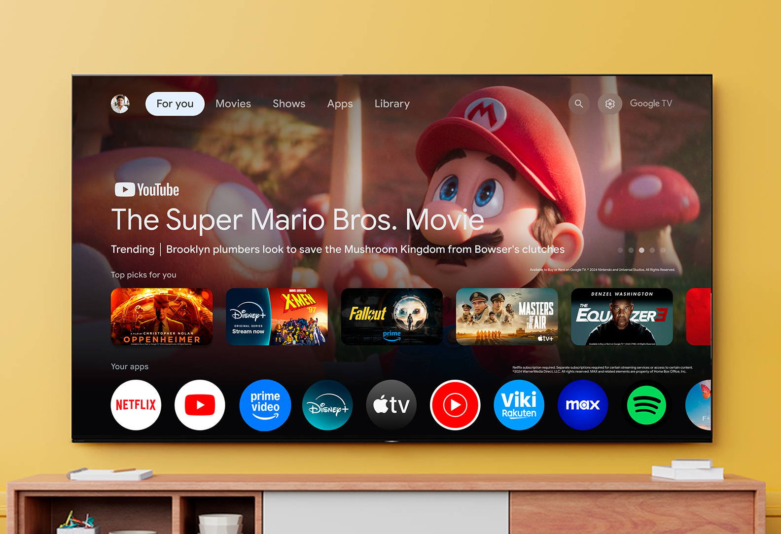 Televisor grande instalado en la pared que muestra la interfaz de Google TV con Super Mario Bros.: la película. Las aplicaciones de streaming se presentan a continuación.
